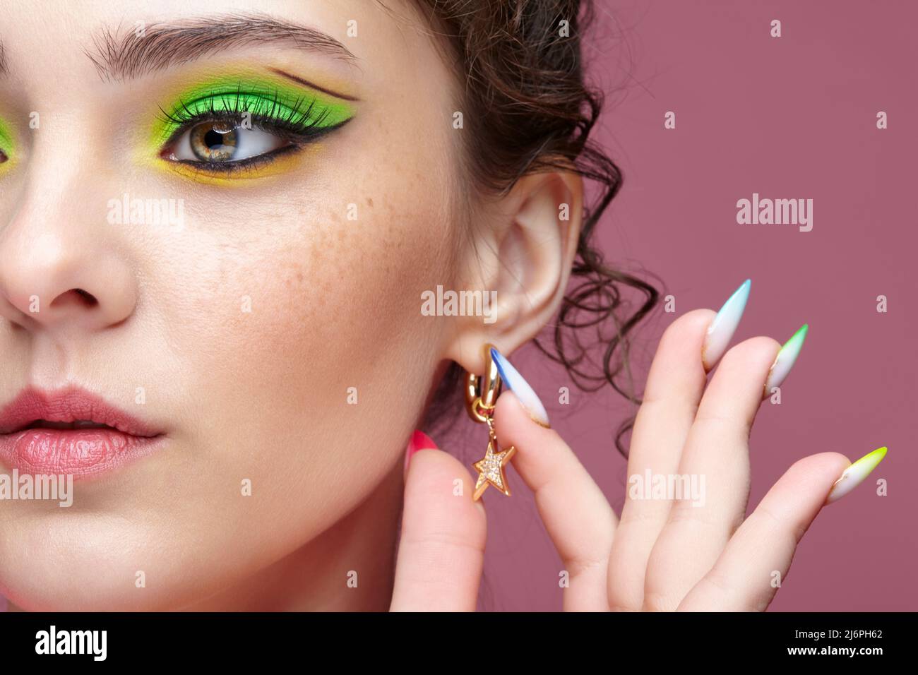 Portrait of young woman touches an earring in the form of a star on her ear. Female with unusual green eyes shadows makeup. Girl with nails with multi Stock Photo