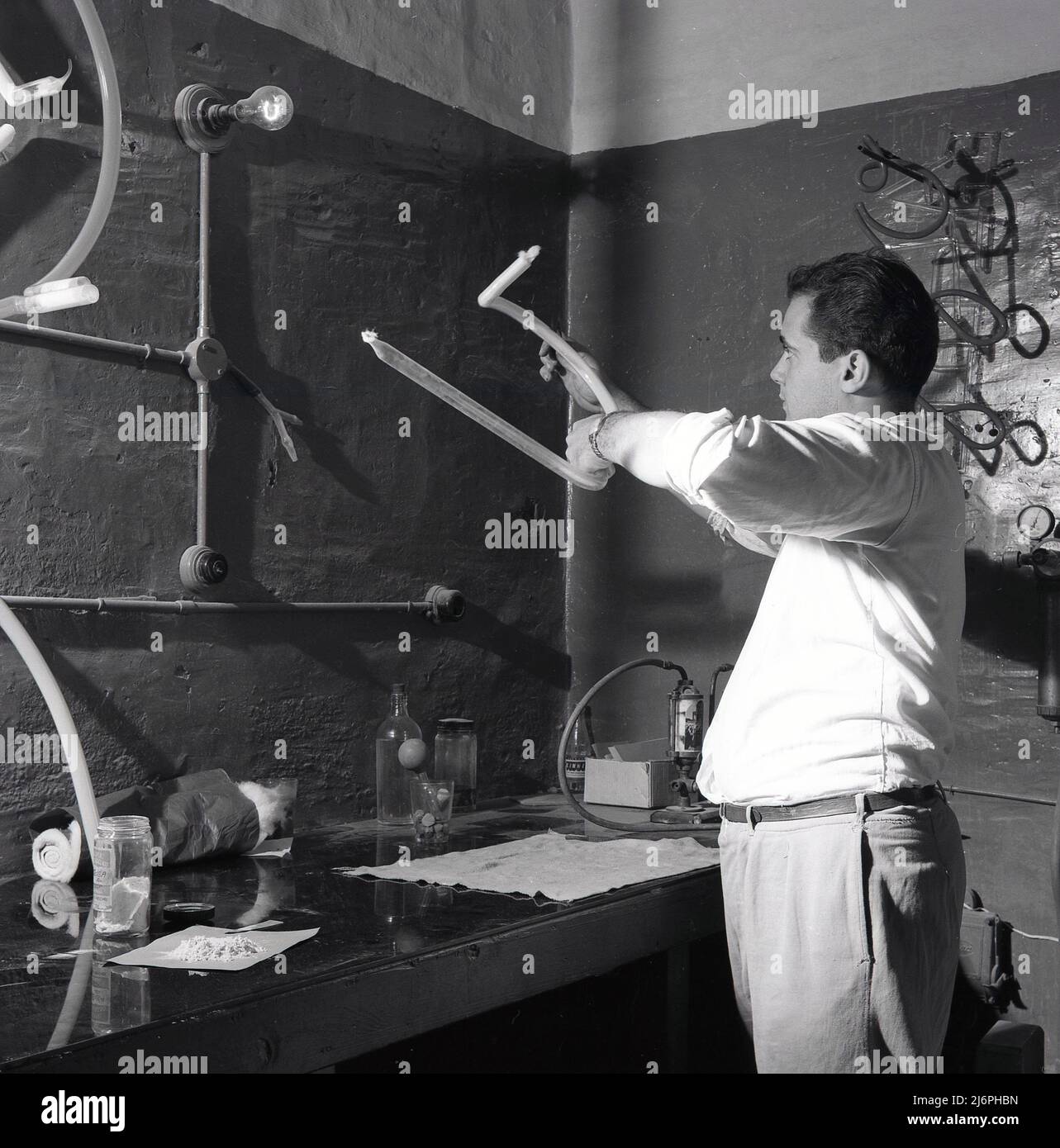 1950s, historical, a man in workshop making neon signs. Made from gas-discharge tubes that contain neon or other gases, these electric signs are produced by a craftsman who can bend glass tubing into shapes and who is known as a glass bender, neon bender or tube bender. The tube is heated into sections using burners. Stock Photo