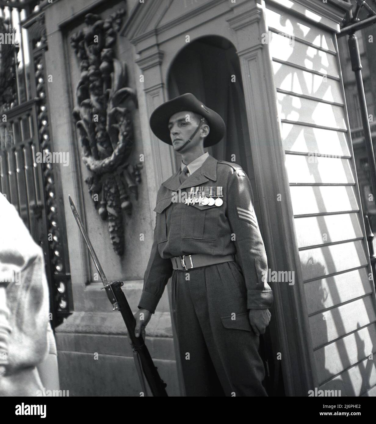 1953, historical, a decorated army sergeant in uniform, with rifle and attached bayonet, possibly Australian, given the hat, manning a sentry post outside Buckingham Palace in Central London during the coronation of Queen Elizabeth II. Stock Photo