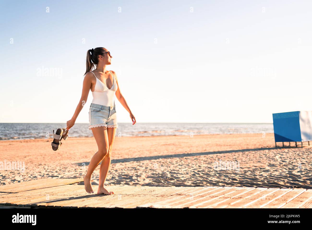 Dancing on the beach at sunset. Playful positive woman walking at sea shore. Summertime freedom, wellness and happy lifestyle. Seaside vacation fun. Stock Photo