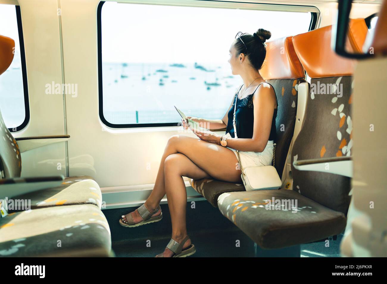 Train travel in summer. Young woman on rail trip in Europe. Railway passenger on journey to vacation destination. Girl looking out the window. Stock Photo