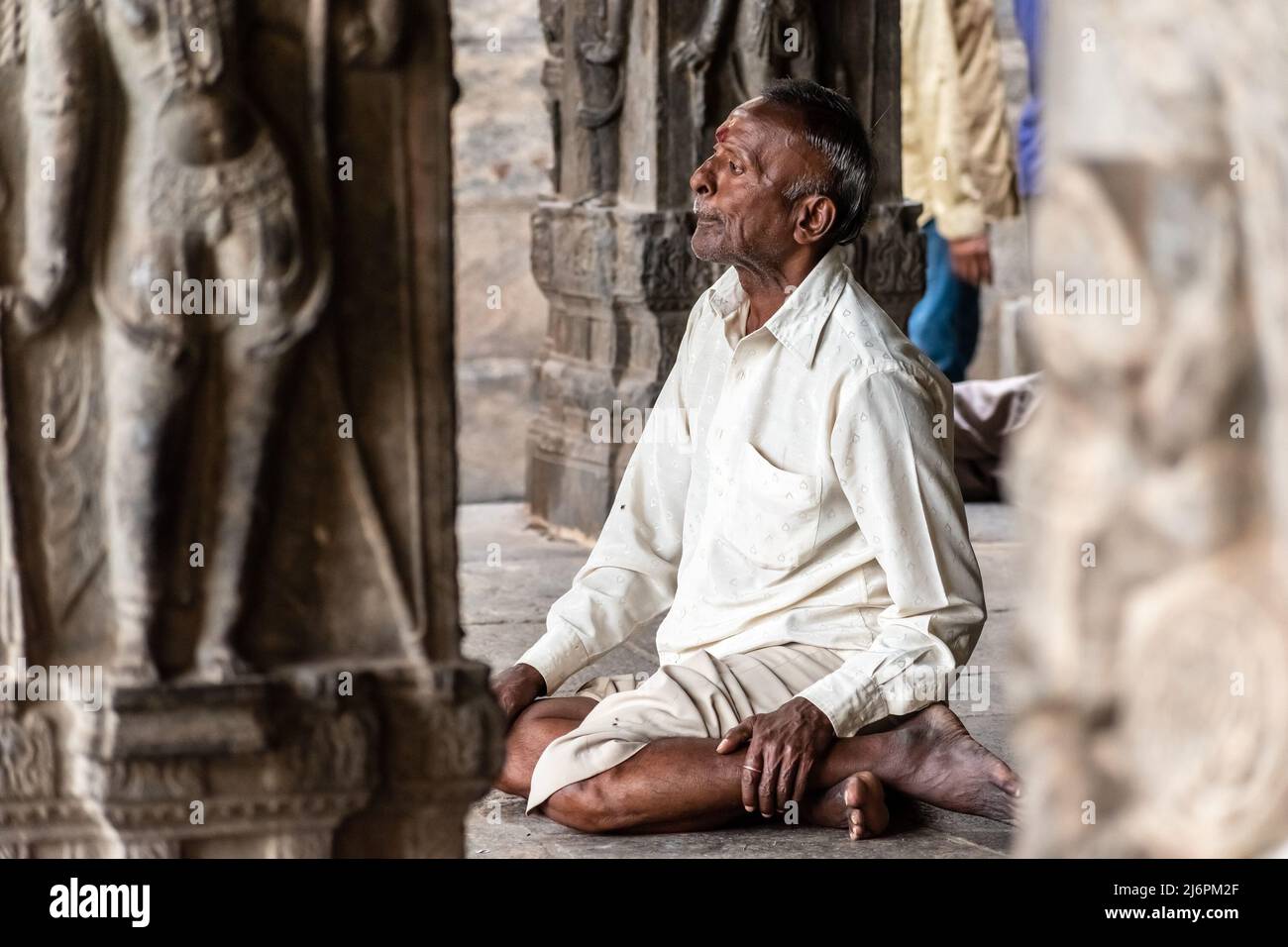 Vellore, Tamil Nadu, India - September 2018: An elderly Indian man sitting cross legged on the stone floor of an ancient Hindu temple in the Vellore F Stock Photo