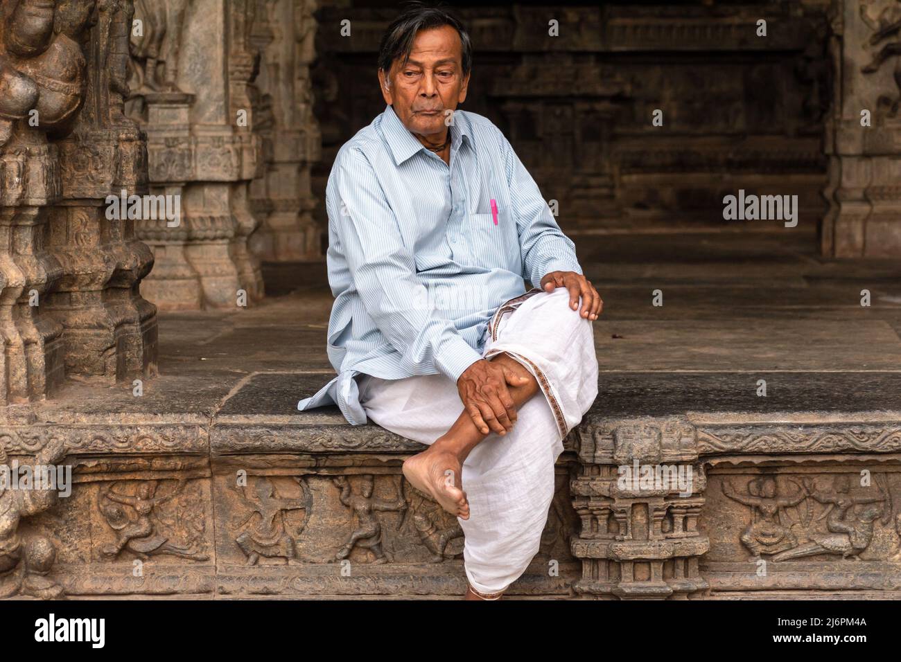 Vellore, Tamil Nadu, India - September 2018: An Indian man wearing a shirt and dhoti sitting cross legged in an ancient Hindu temple in the Vellore fo Stock Photo