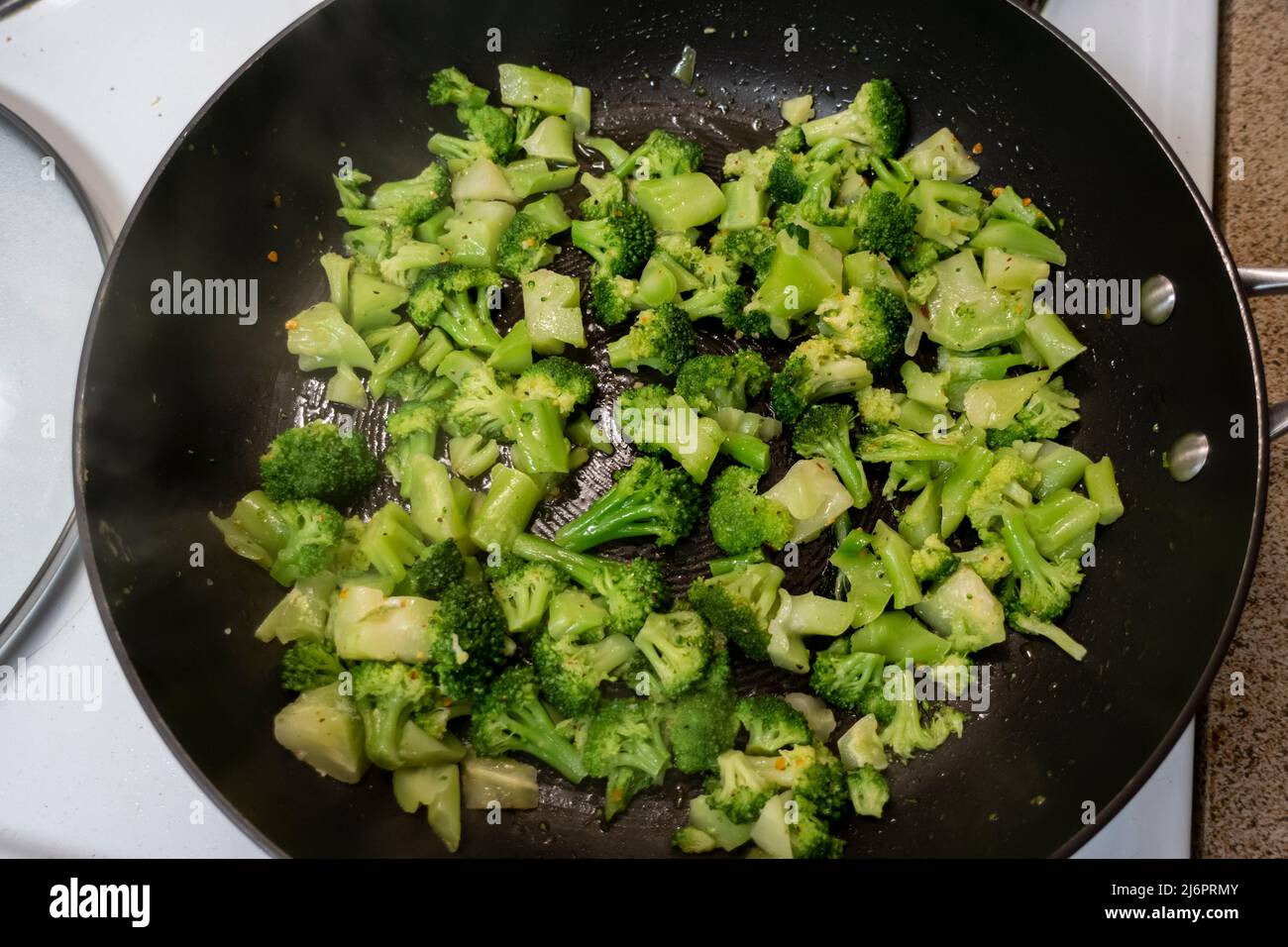 Top down view of chopped up, frozen broccoli cooking in a large black skillet on a white stove