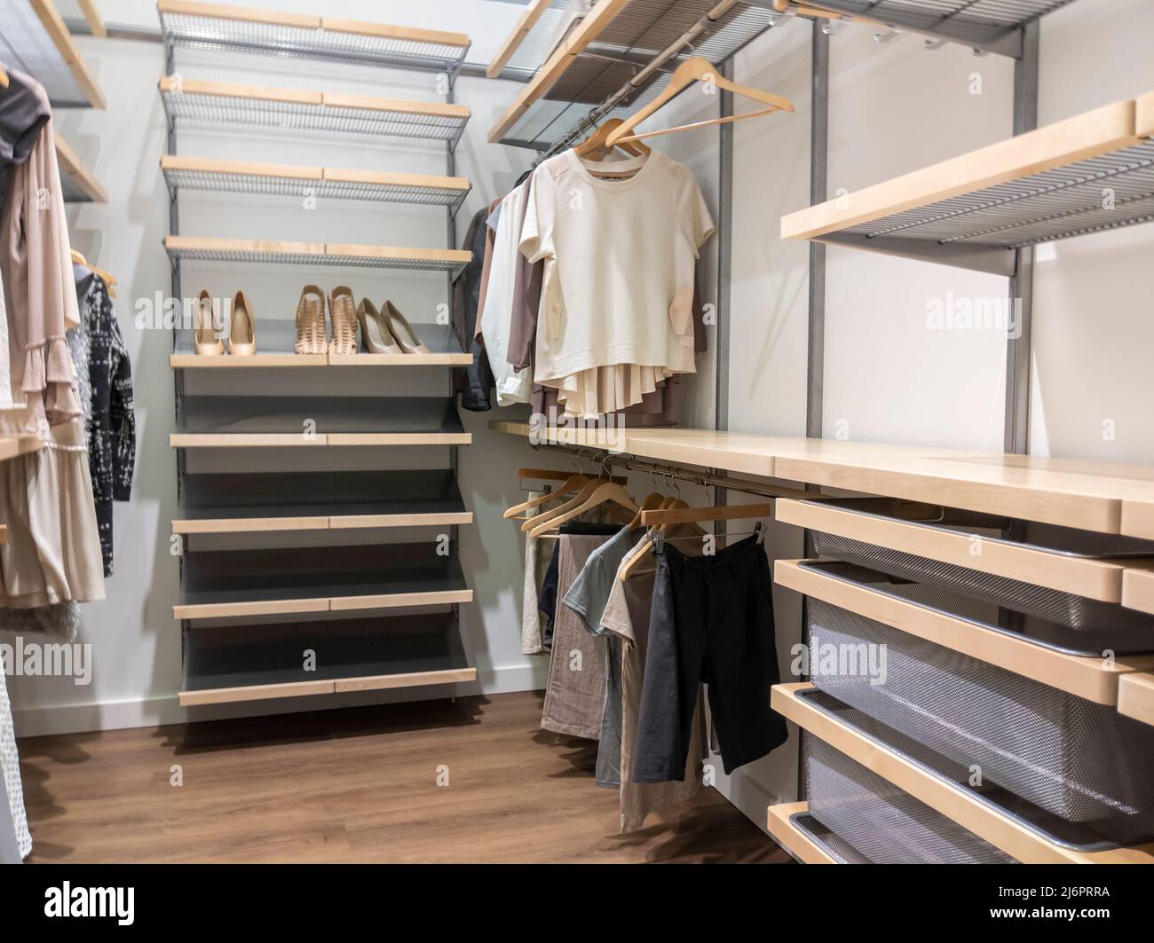 A large, walk in closet with shirts and pants hanging up on hangers and shoes on the shelving Stock Photo