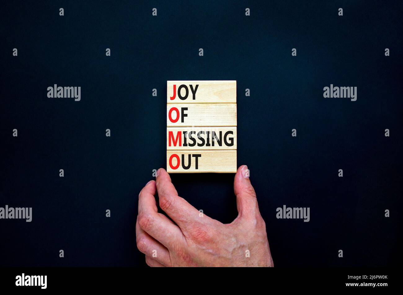 JOMO joy of missing out symbol. Concept words JOMO joy of missing out on wooden blocks on a beautiful black background. Businessman hand. Business JOM Stock Photo