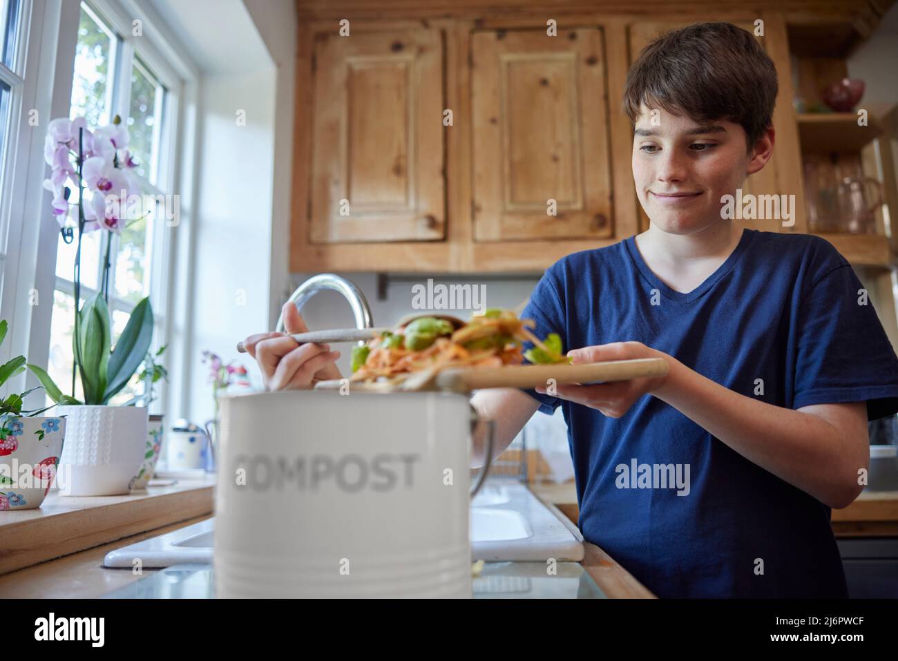 Boy In Kitchen Making Compost Scraping Vegetable Leftovers Into Bin Stock Photo