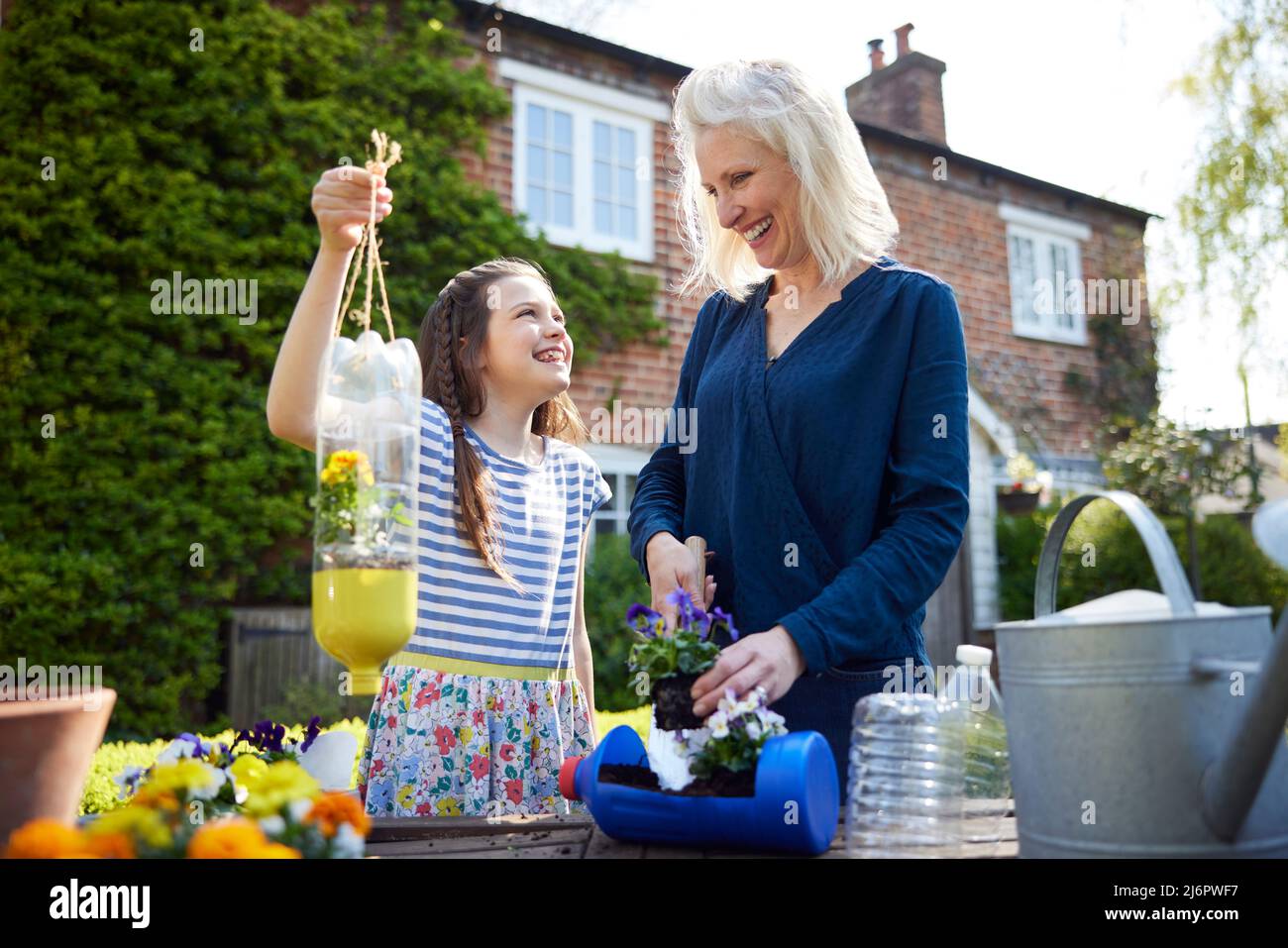 Mother And Daughter Making Recycled Plant Holders From Plastic Bottle Packaging Waste In Garden At Home Stock Photo