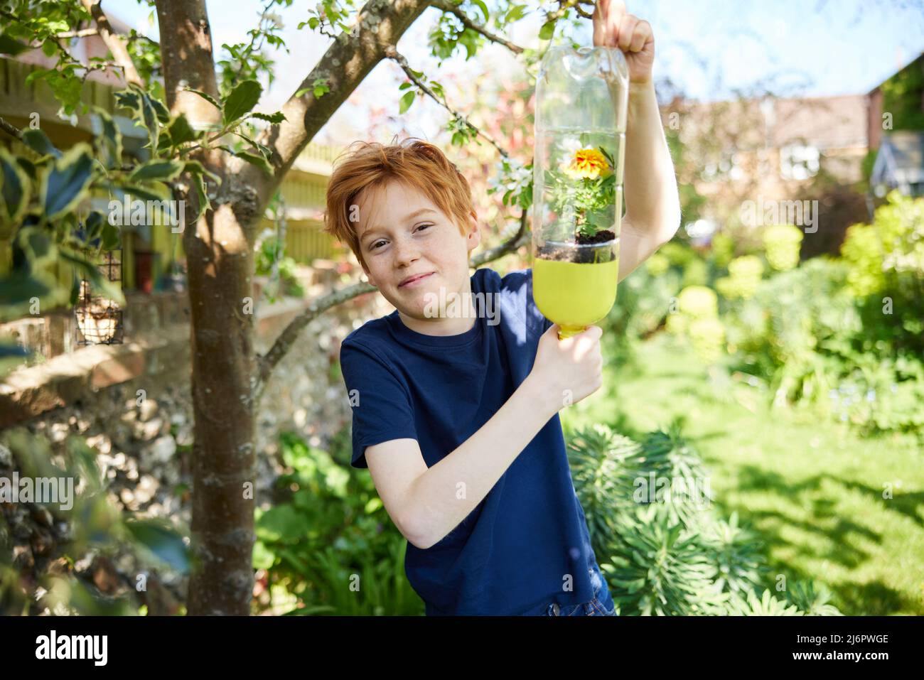 Portrait Of Boy Making Recycled Plant Holder From Plastic Bottle Waste In Garden At Home Stock Photo