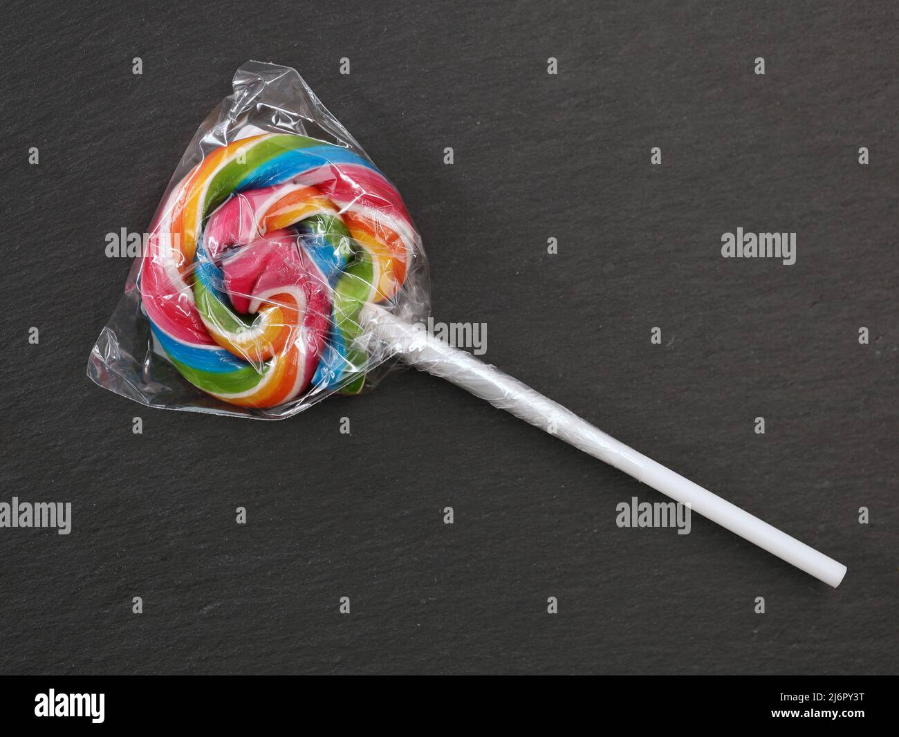single colorful lollipop wrapped in plastic packaging on black ...