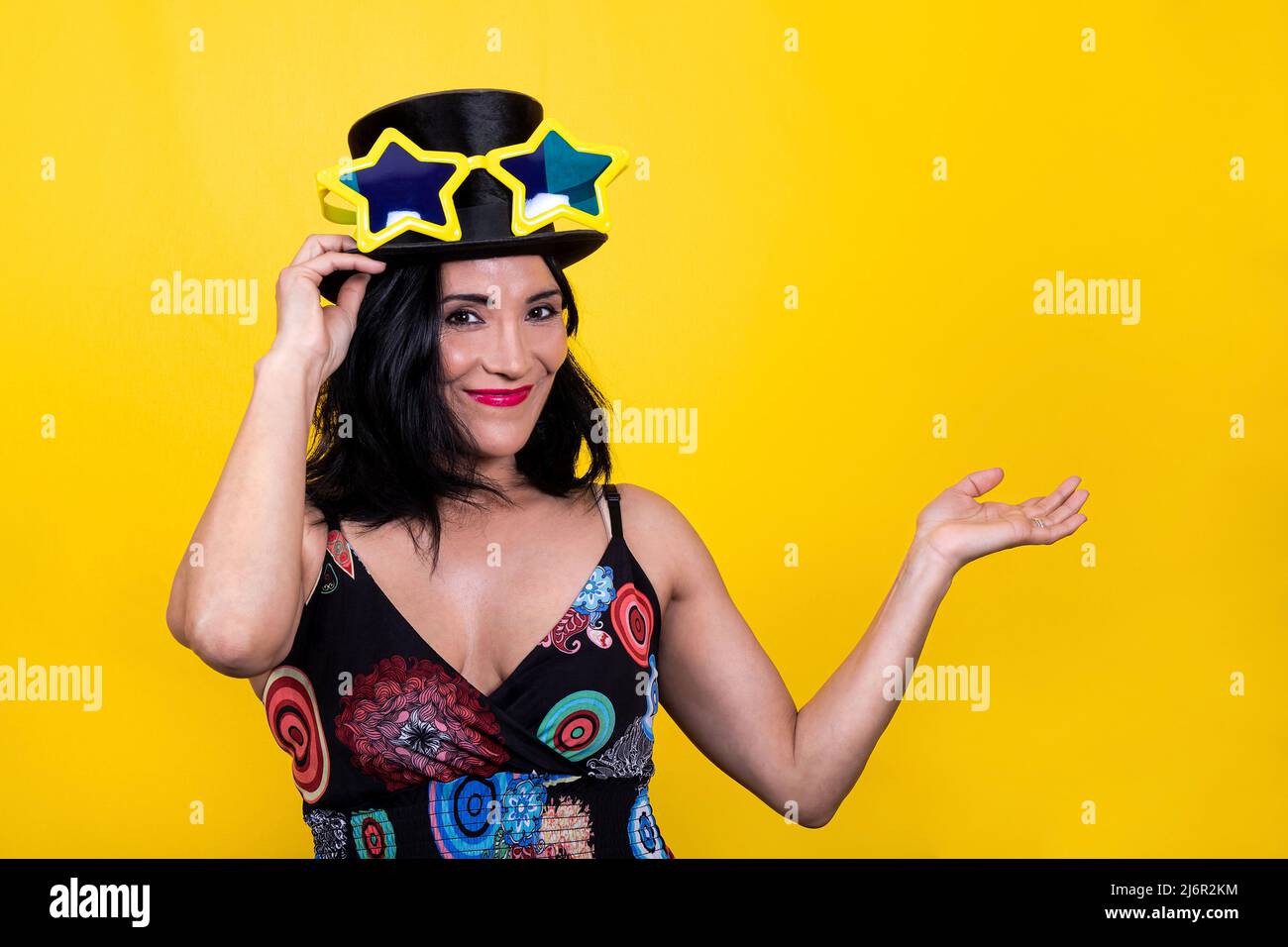 Beautiful woman wears star-shaped yellow glasses and a top hat. The young brunette woman is happy and having fun at the party. Stock Photo