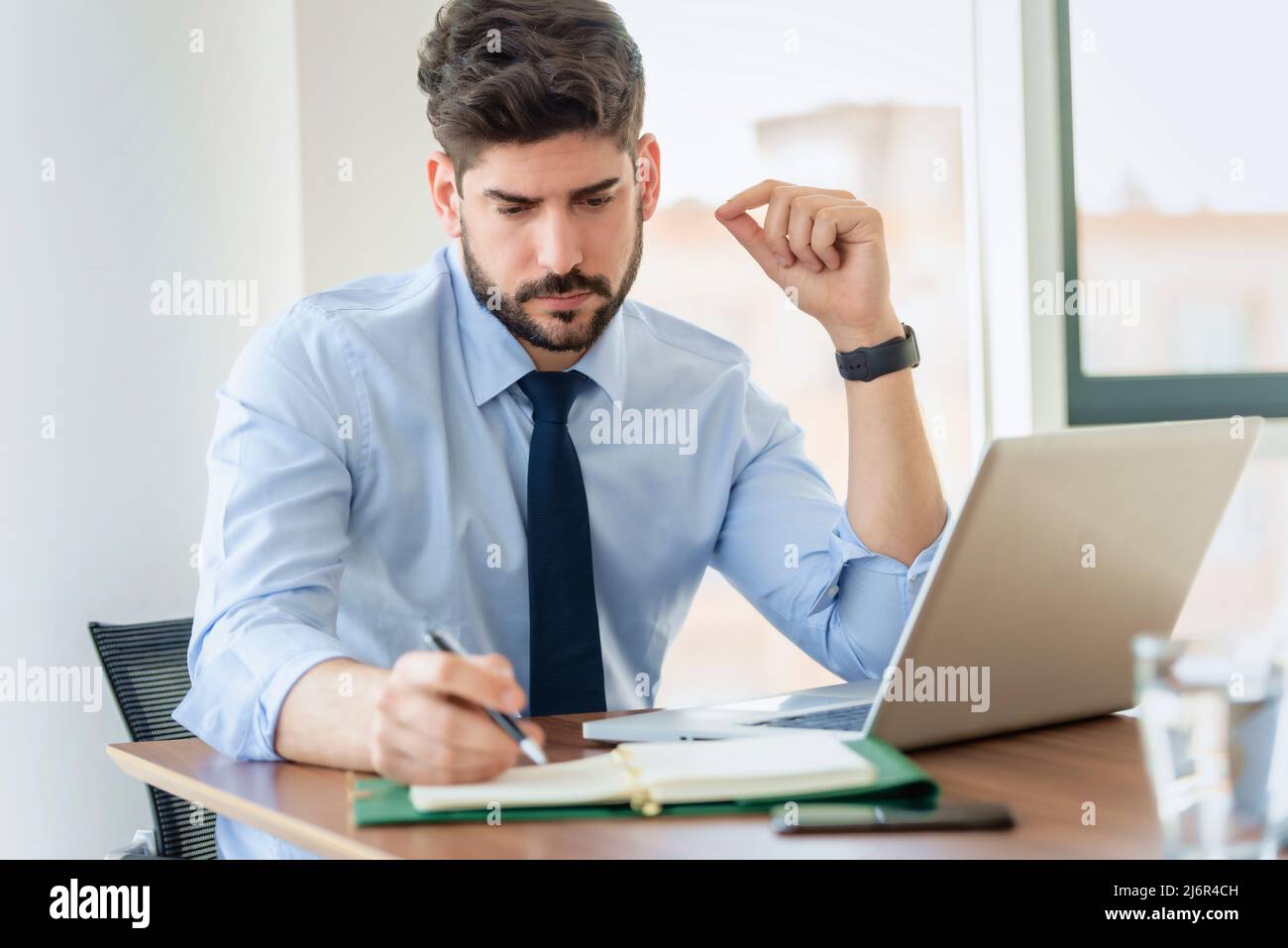 Thinking businessman using laptop and making notes while working at the office. Stock Photo