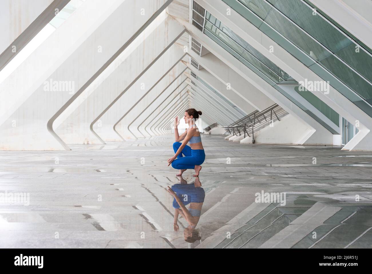 woman practices yoga asana Toe Balance pose outdoors against the background of modern urban architecture. Stock Photo