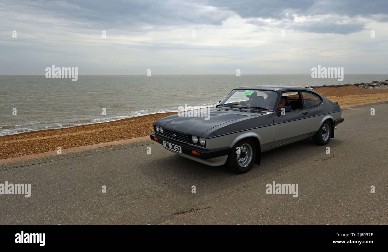 Classic Grey and Silver Ford Capri being driven along seafront promenade beach and sea in background. Stock Photo