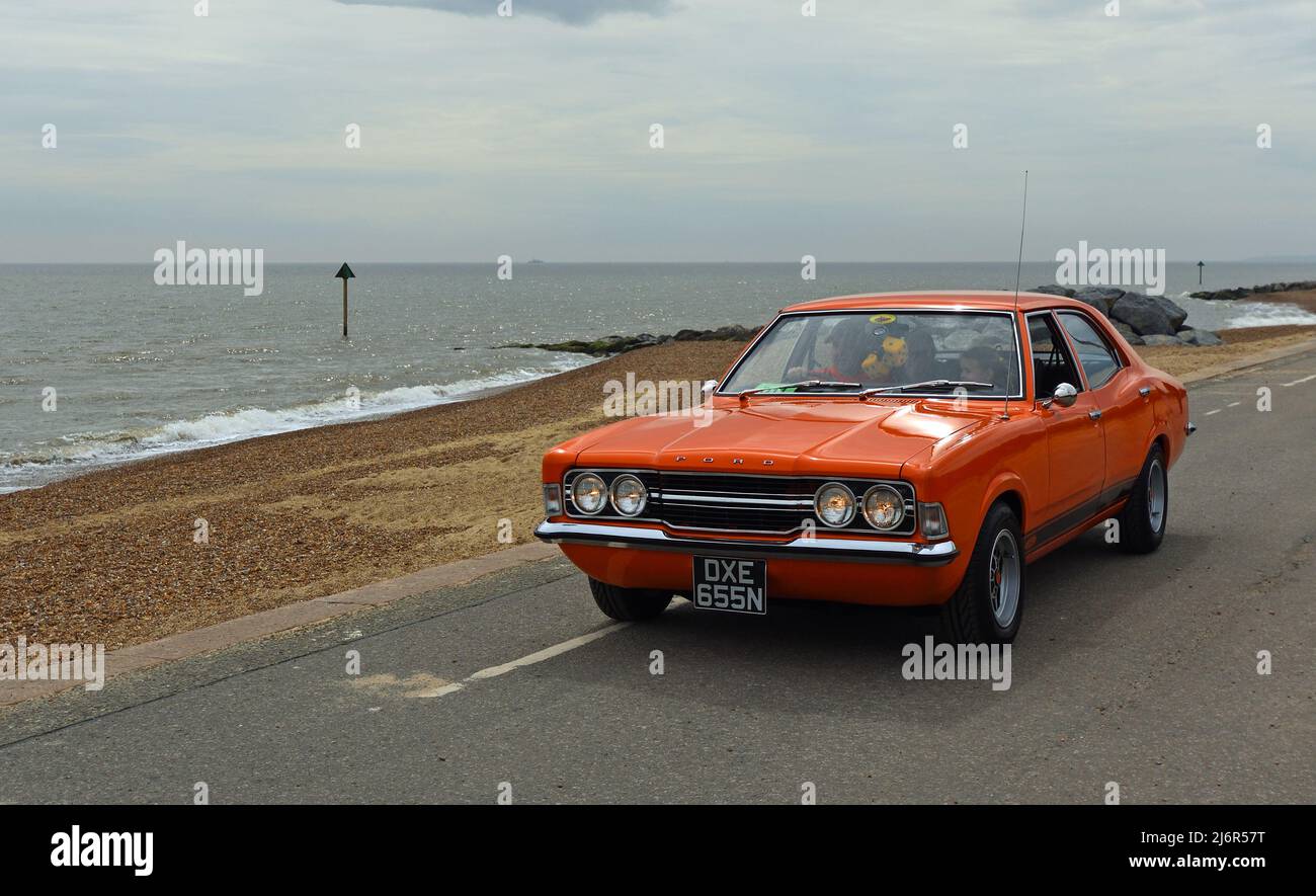 Classic Orange Ford Cortina MK3 Car being driven along seafront promenade beach and sea in background. Stock Photo