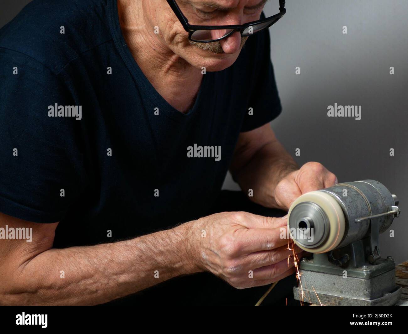 Old man is sharpening a tool using electrical grinding machine, selective focus Stock Photo