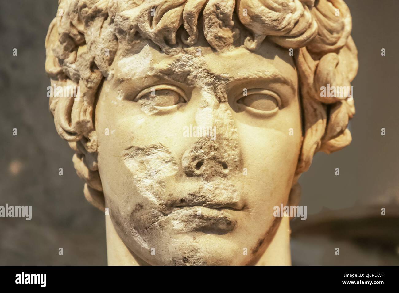 Close-up of head of ancient marble statue of attractive Greek youth with parts of face chipped off and destroyed Stock Photo