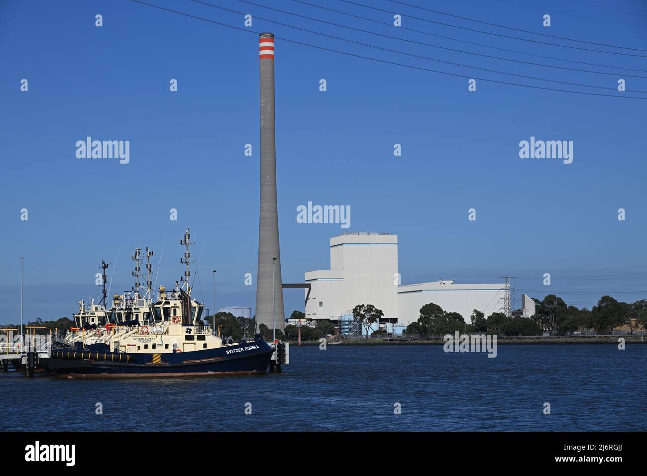 Docked tug boat Svitzer Eureka, alongside other tug boats on the Yarra River, with Newport Power Station in the background across the river Stock Photo