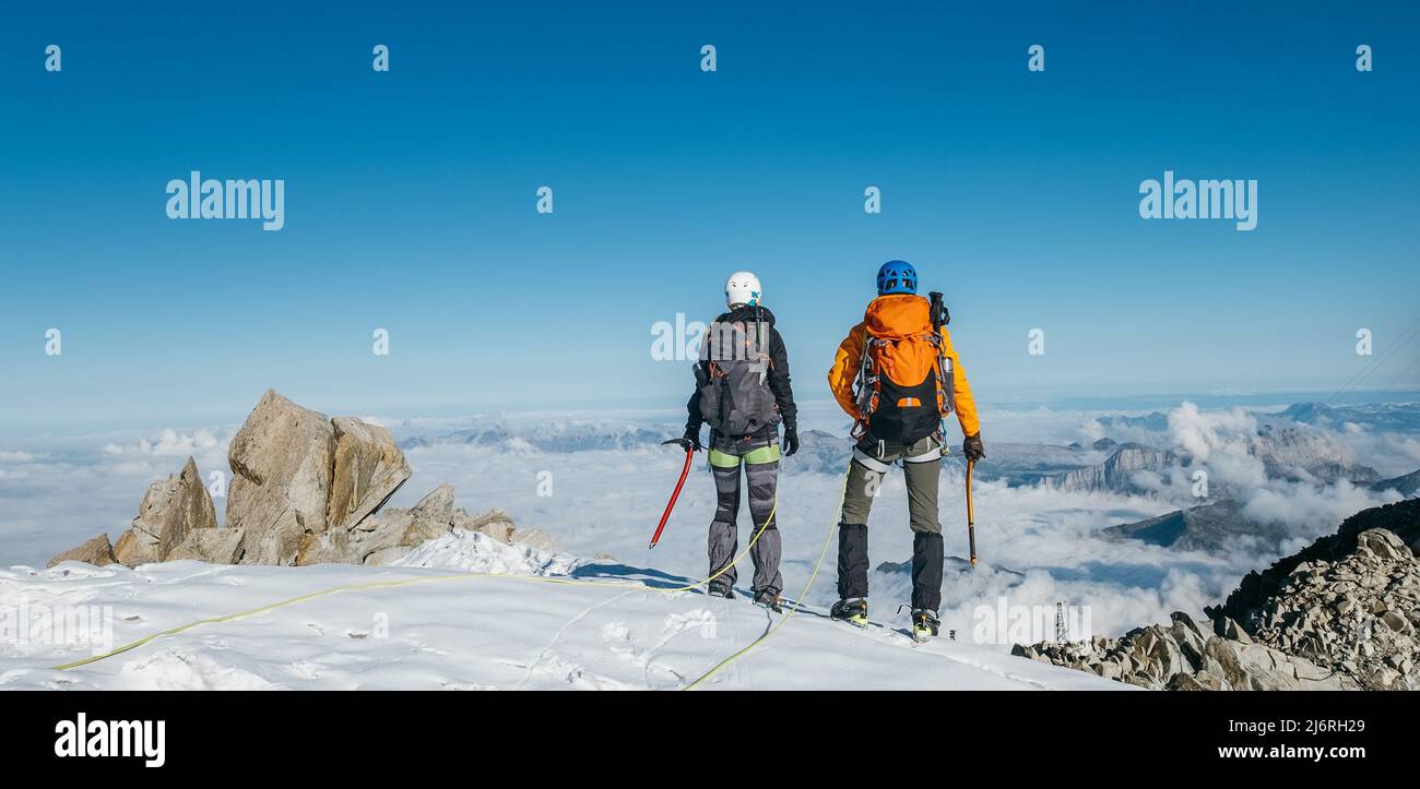 Couple connected team rope  with climbing harness dressed mountaineering clothes with backpacks and ice axes enjoying views ascending Mont Blanc (Mont Stock Photo