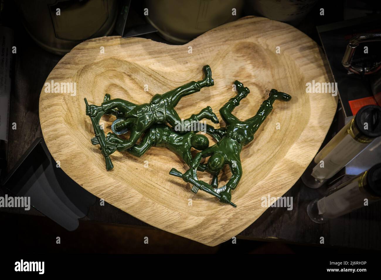 Green plastic toy army men with rifles over head piled in wooden heart dish on shelf with other items - overhead view Stock Photo