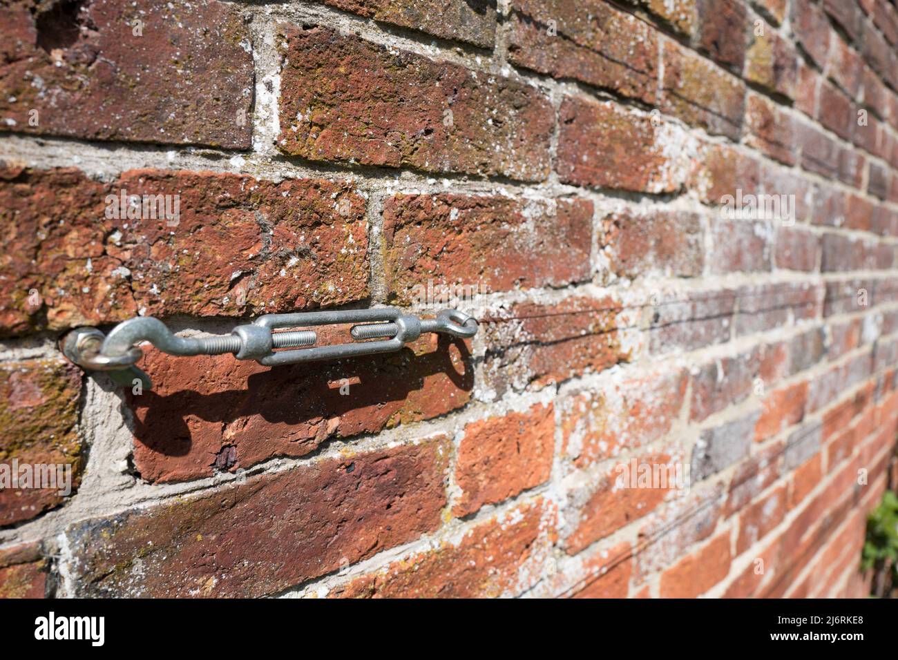 Standard galvanised steel Turnbuckle with hook and shackle attached to a brick wall with wire attached. Stock Photo