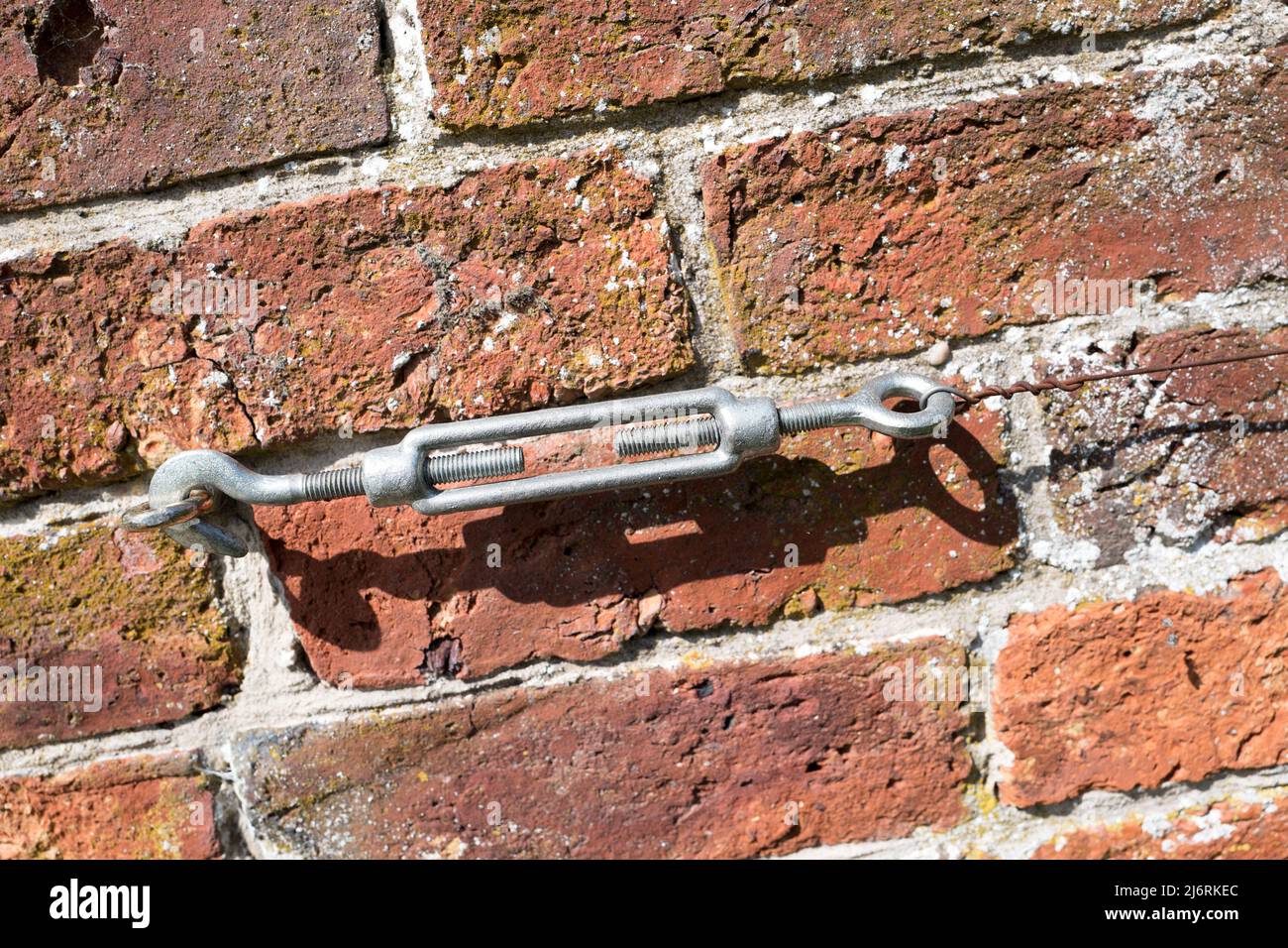Standard galvanised steel Turnbuckle with hook and shackle attached to a brick wall with wire attached. Stock Photo