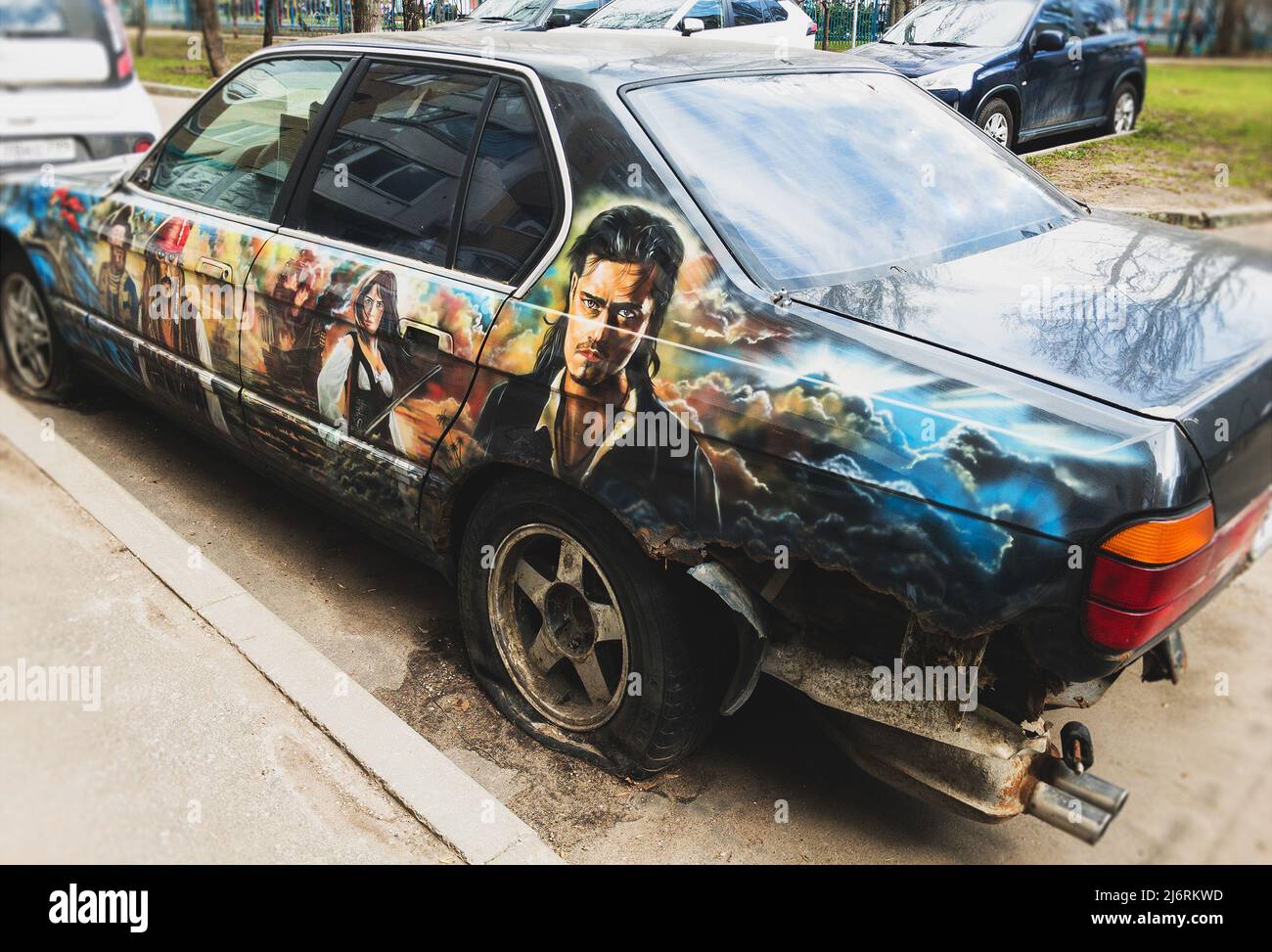 abandoned rusty car painted with film stars is parked in a residential area Stock Photo