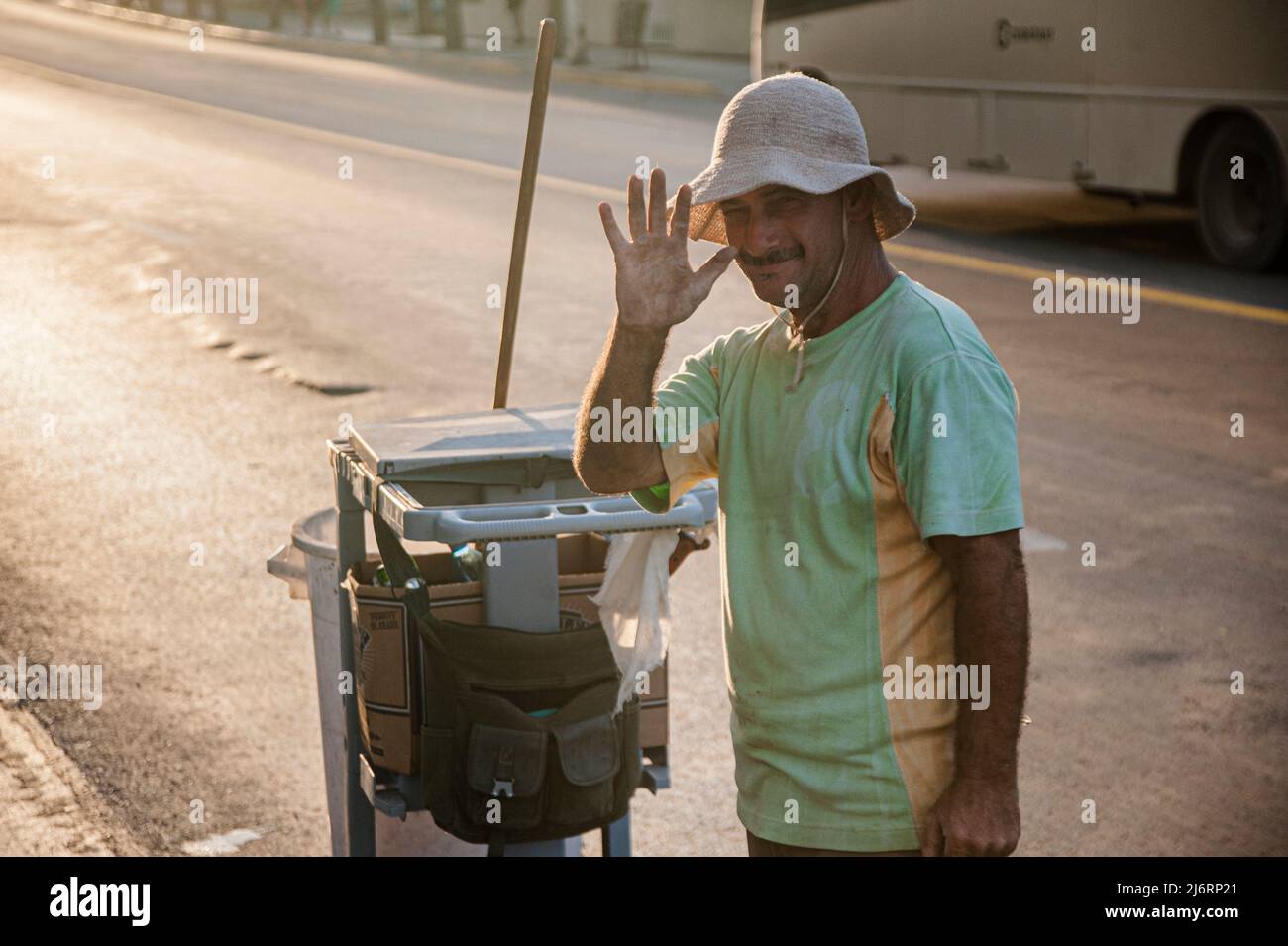 Cuban street cleaner smiles and waves at the camera during sunset of and orange colored sky in Varadero, Cuba. Stock Photo
