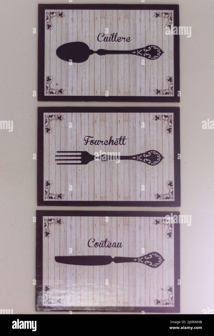 three cream and black paintings with drawings of a fork, knife and spoon, with the descriptions written in french on a kitchen wall Stock Photo