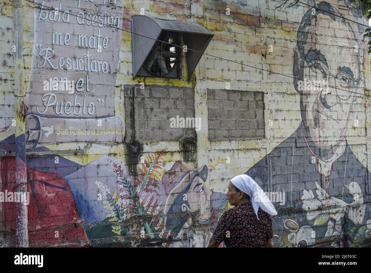 A woman stands near a mural depicting Saint Oscar Romero in Panchimalco. Stock Photo