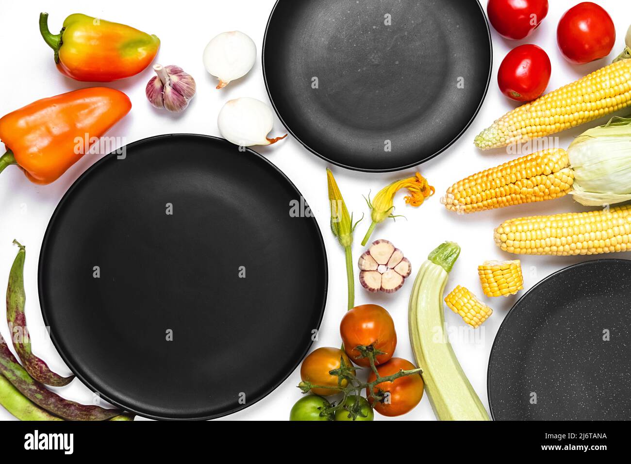Creative layout made of autumn vegetables. Tomatoes, onion, carrot, garlic, red beet, pepper, zucchini, corn, green haricot and black plate on white s Stock Photo