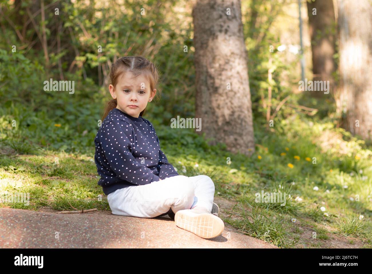 Little beautiful girl sits on a stone surface in a park on a blurred
