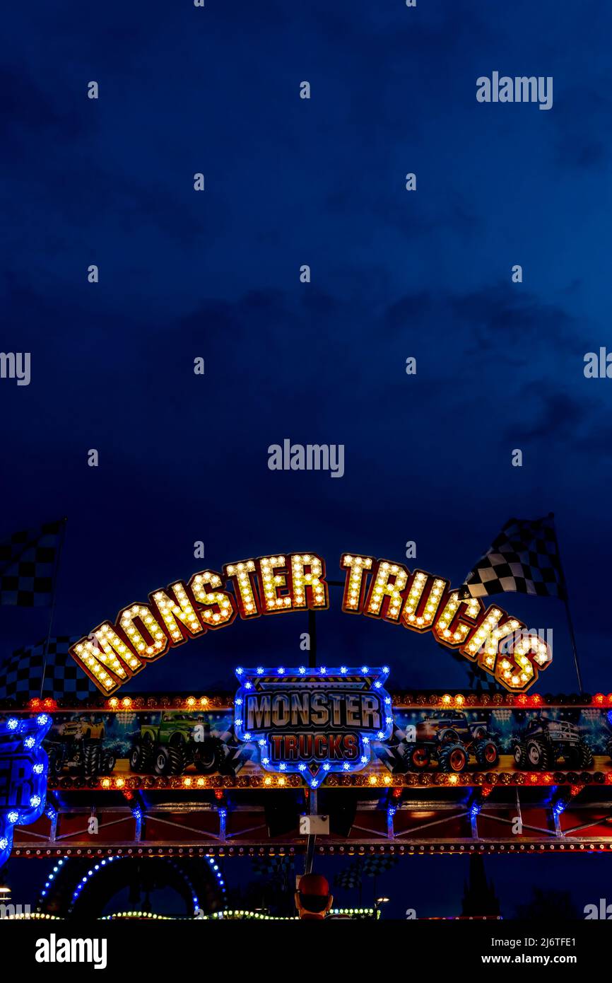 The lights of the Monster Trucks fairground ride brighten the night sky. Stock Photo