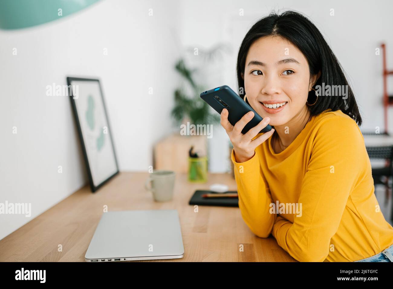 Woman sending a voice message on mobile phone during a break from work at home. Stock Photo