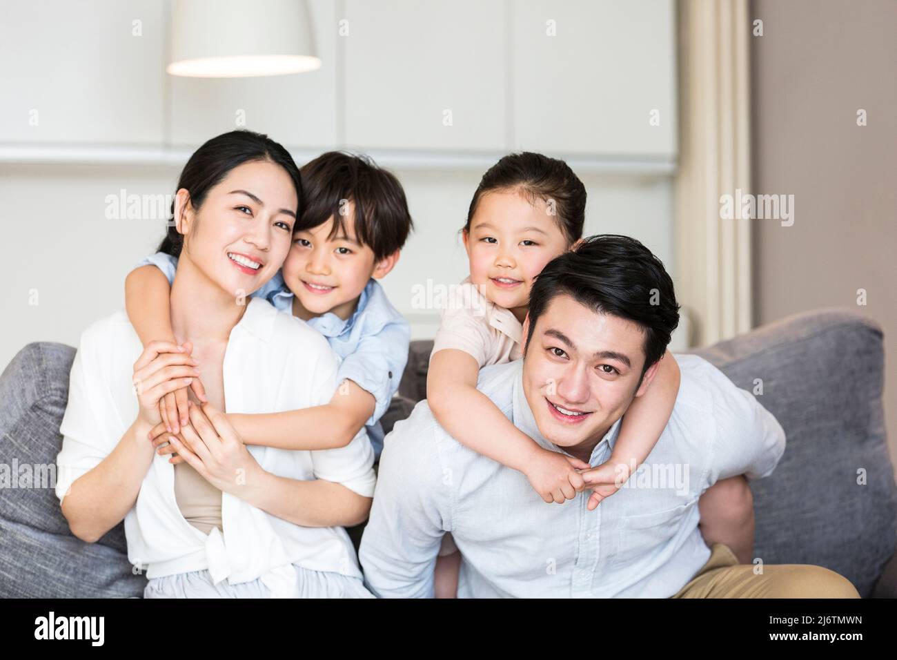 The father carries his daughter on his back, the son hugs the mother from behind, and the harmonious family plays on the sofa - stock photo Stock Photo