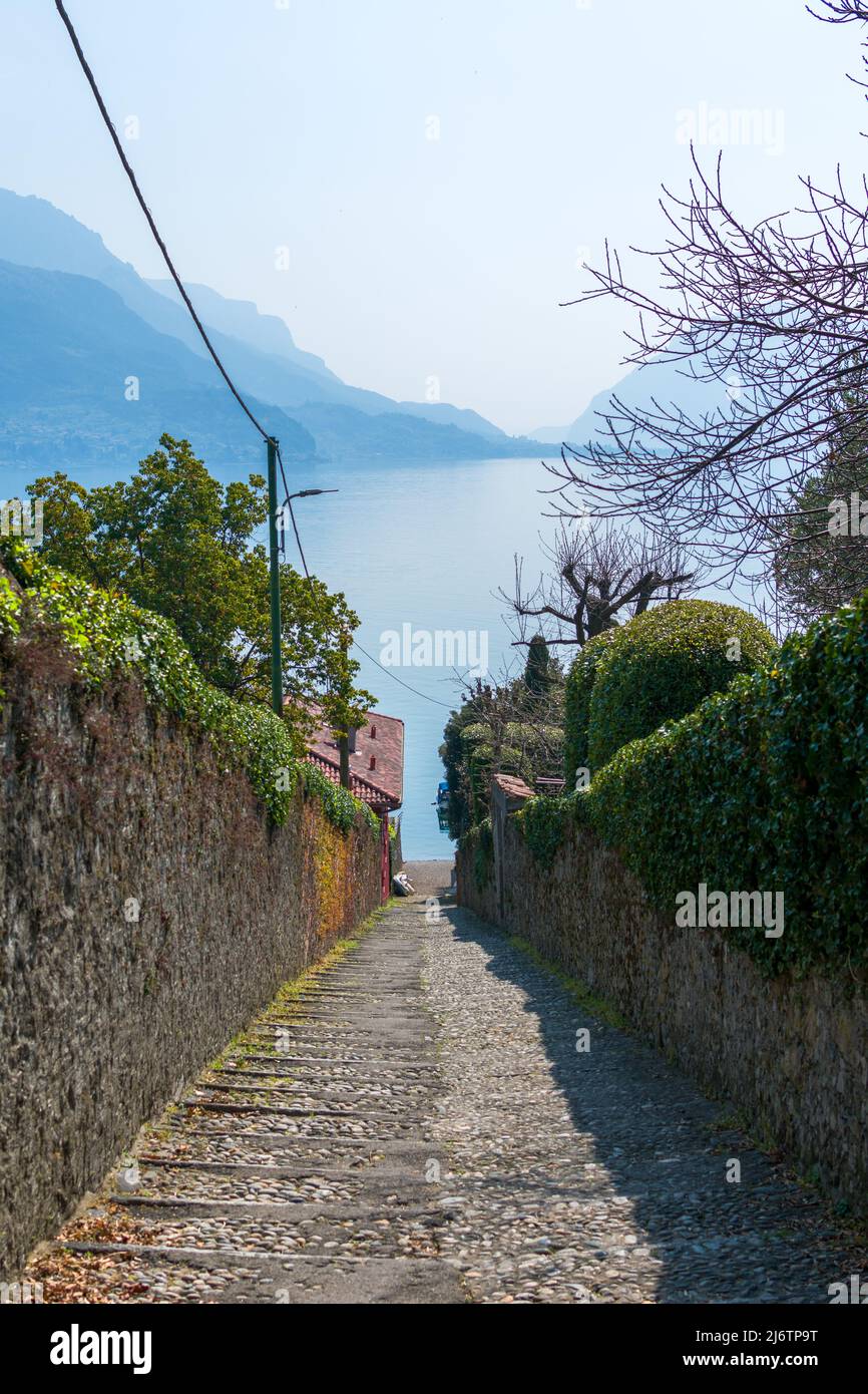 A bright sunny day in Lake Como Lago di Como, a pathway down to the water and blue mountains reflection a mesmerizing fantasy landscape North Italy Stock Photo