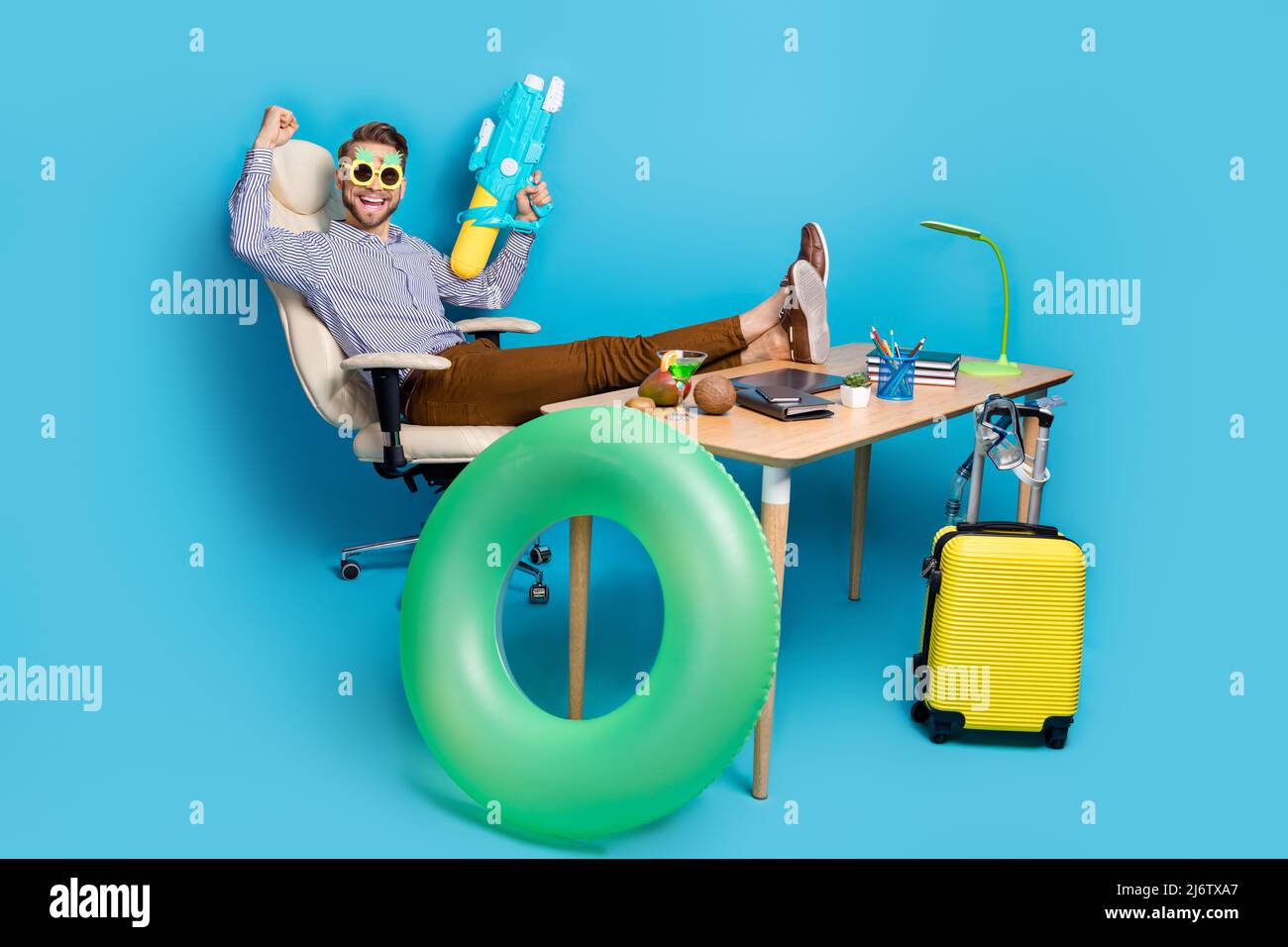 Full length of delighted crazy person sit chair raise fist hold water pistol isolated on blue color background Stock Photo