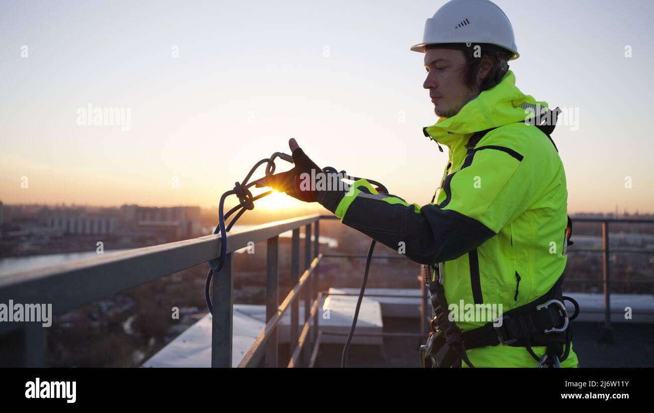 Industrial climber removes safety equipment from roof fence at sunset ...