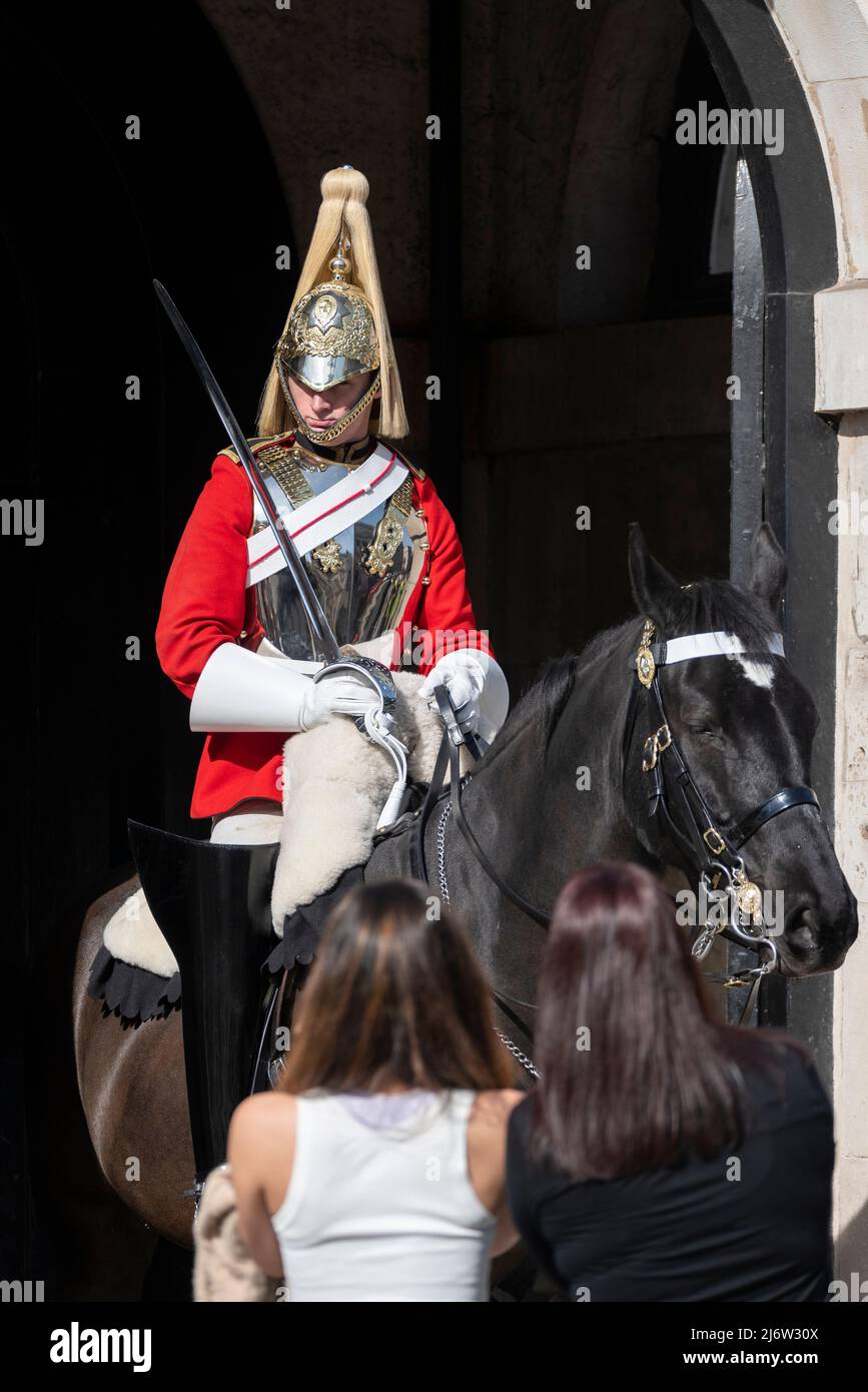 British Army Life Guards of Household Cavalry soldier on ceremonial mounted guard duty at Horse Guards, London, UK. Female tourists viewing trooper Stock Photo