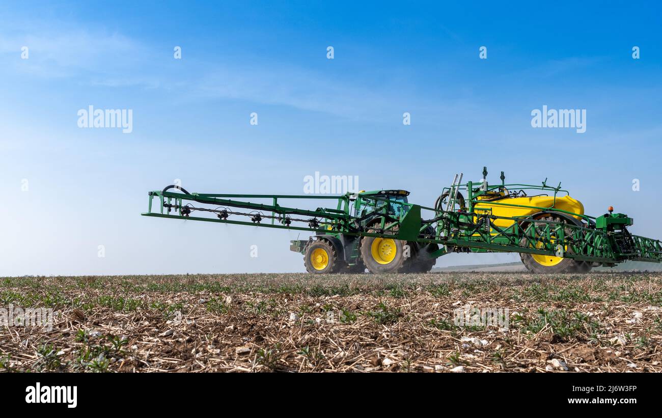 Spraying arable crop on the Yorkshire Wolds near York, using a John Deere 6215 tractor and a towed John Deere R952i sprayer. Stock Photo