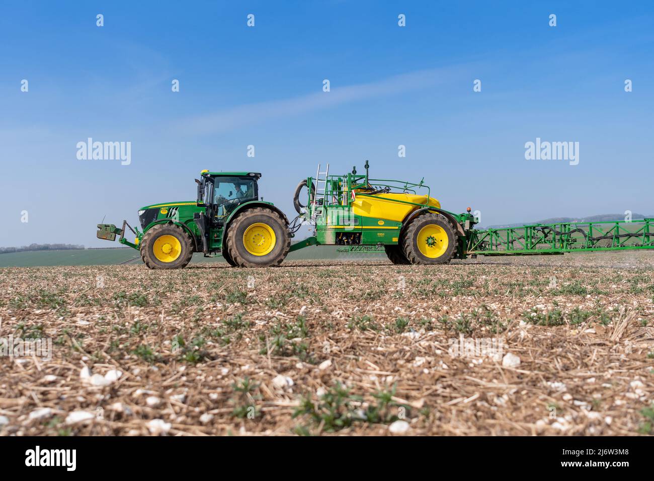 Spraying arable crop on the Yorkshire Wolds near York, using a John Deere 6215 tractor and a towed John Deere R952i sprayer. Stock Photo