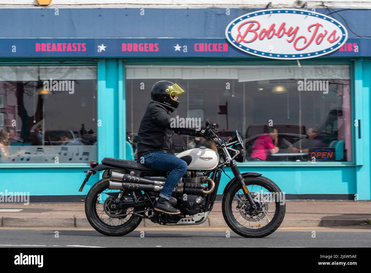 British Triumph bike passing American diner at the Southend Shakedown 2022 motorcycle event on Easter Bank Holiday Monday in Southend on Sea, UK. Stock Photo