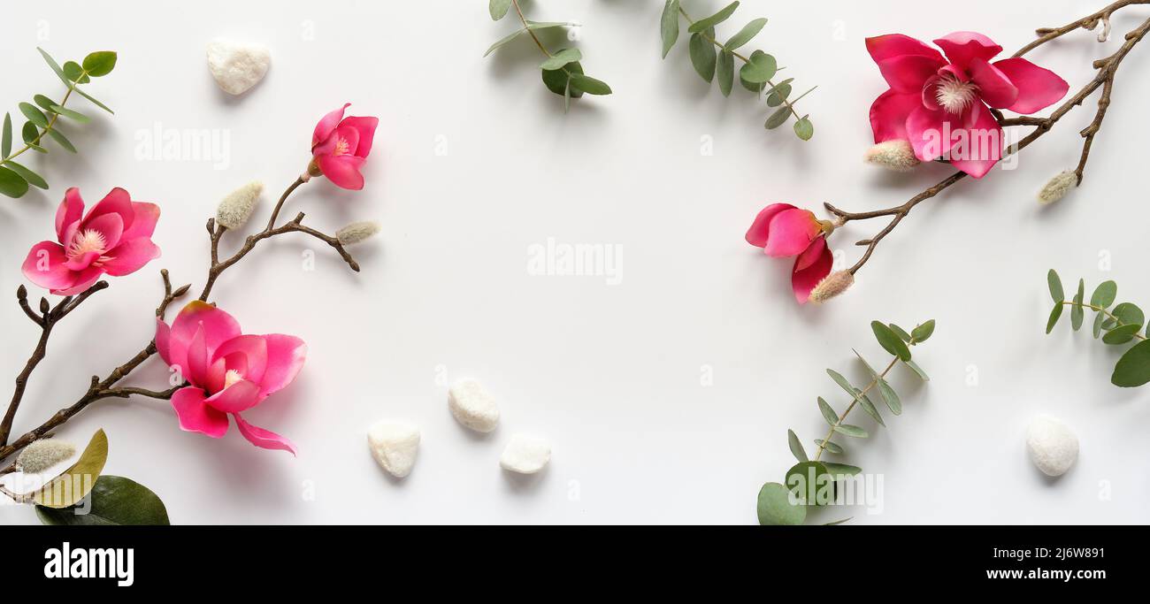 Pink magnolia flowers on twigs, fresh eucalyptus leaves. Blank pink card with grey envelope. Stock Photo
