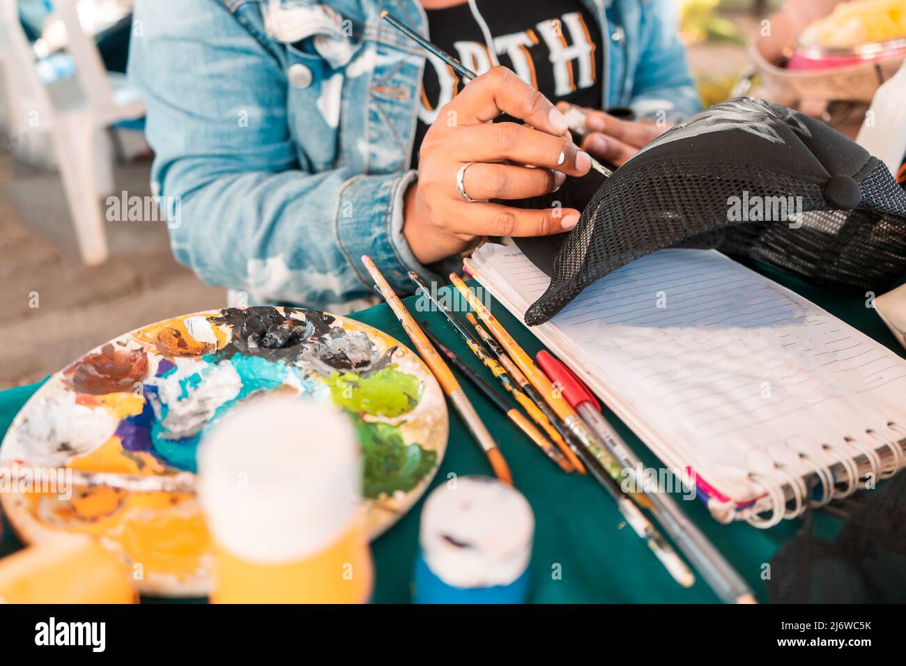 Closeup to the hands of a Latin woman customizing a cap with a brush and paint. Concept of art and entrepreneurship Stock Photo