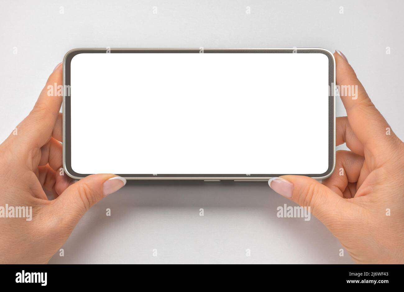 phone mockup in horizontal position. close up hands hold cellphone on gray background. Close up of horizontal black smartphone with blank screen in wo Stock Photo