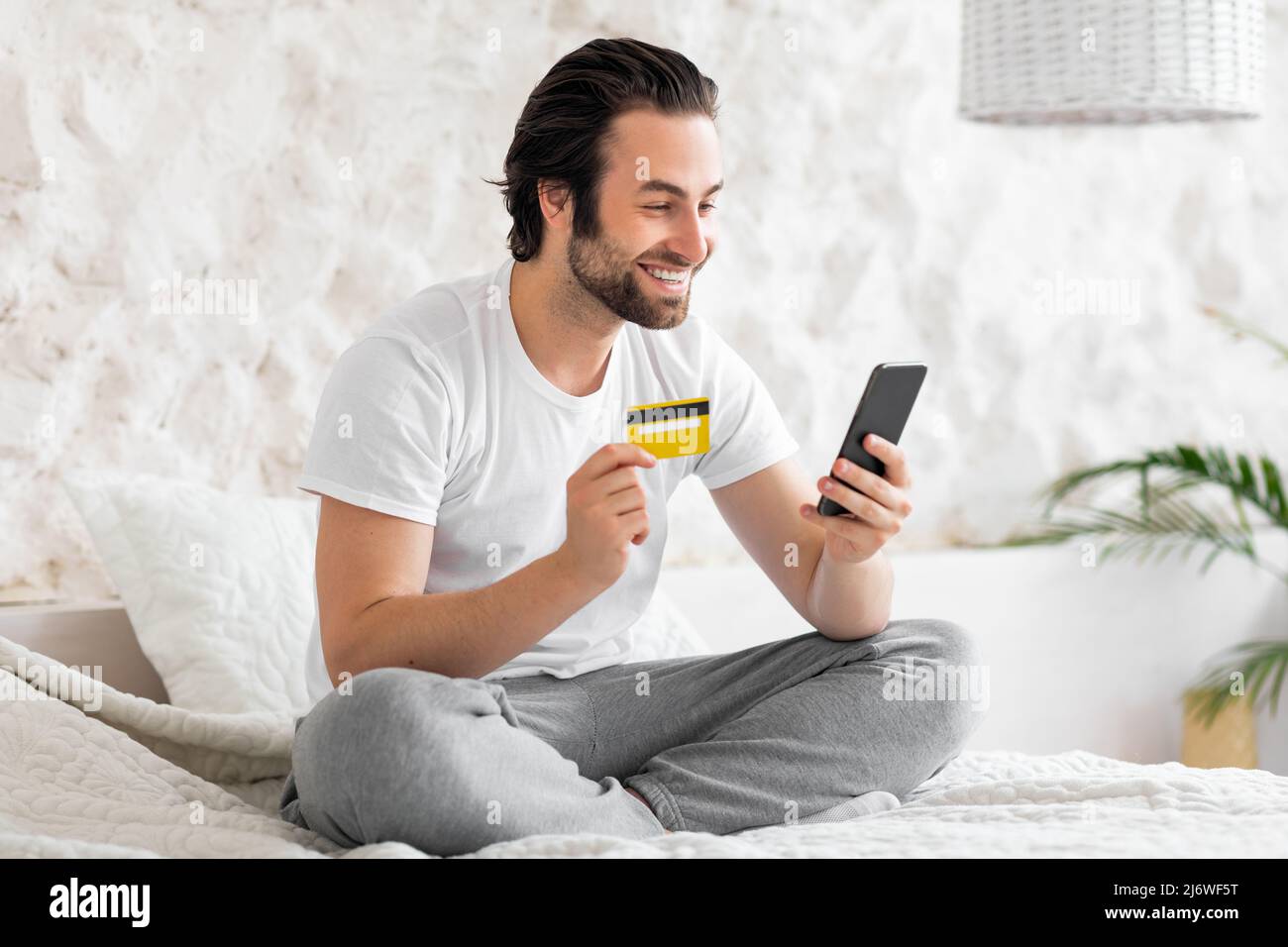 Positive young man shopping on internet, using phone Stock Photo