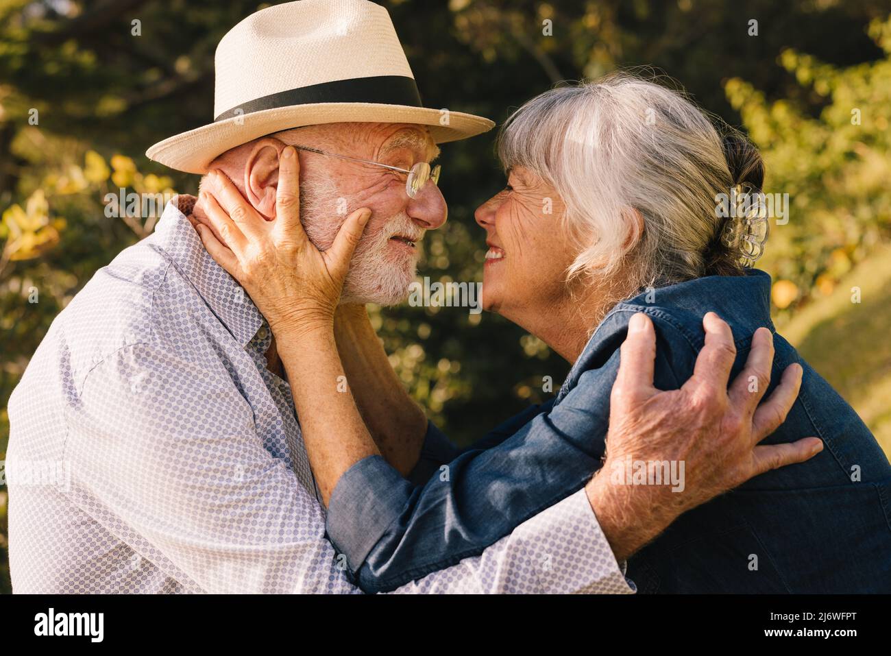 Happy senior couple smiling at each other with love and affection. Grey-haired couple sharing a romantic moment while standing in a park. Cheerful eld Stock Photo