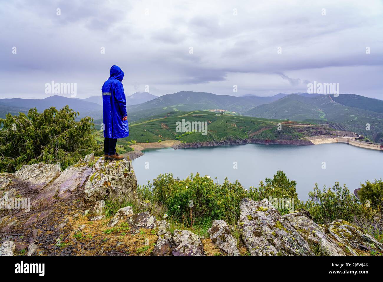 Man climbed a rock on the peak of the mountain and contemplating the valley with the lake. Stock Photo