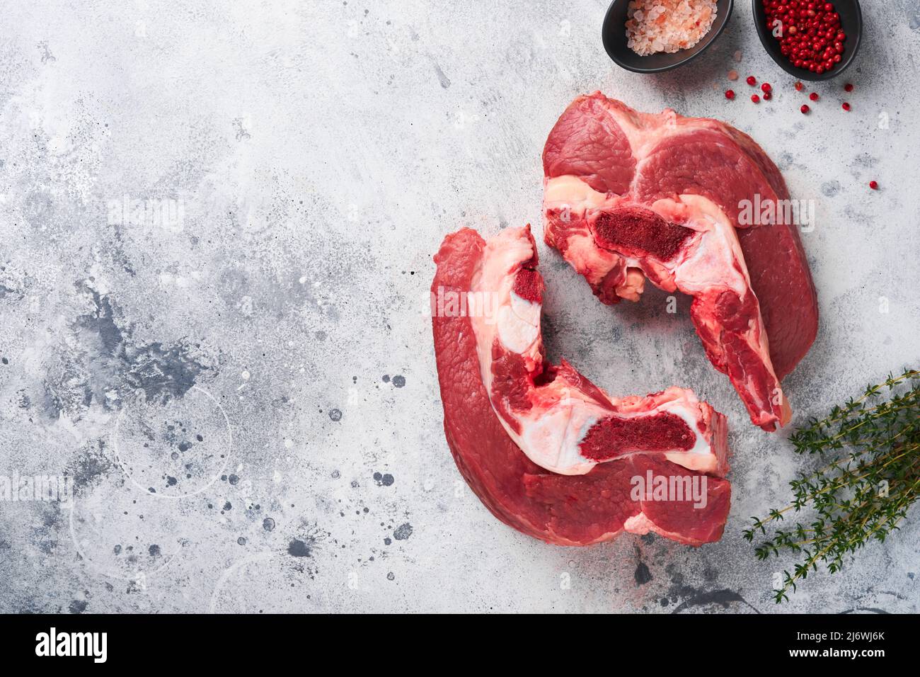 Raw beef meat. Rough piece of meat on bone for roast or soup with salt, pepper, thyme and rosemary on old grey concrete table background. Entrecote. R Stock Photo