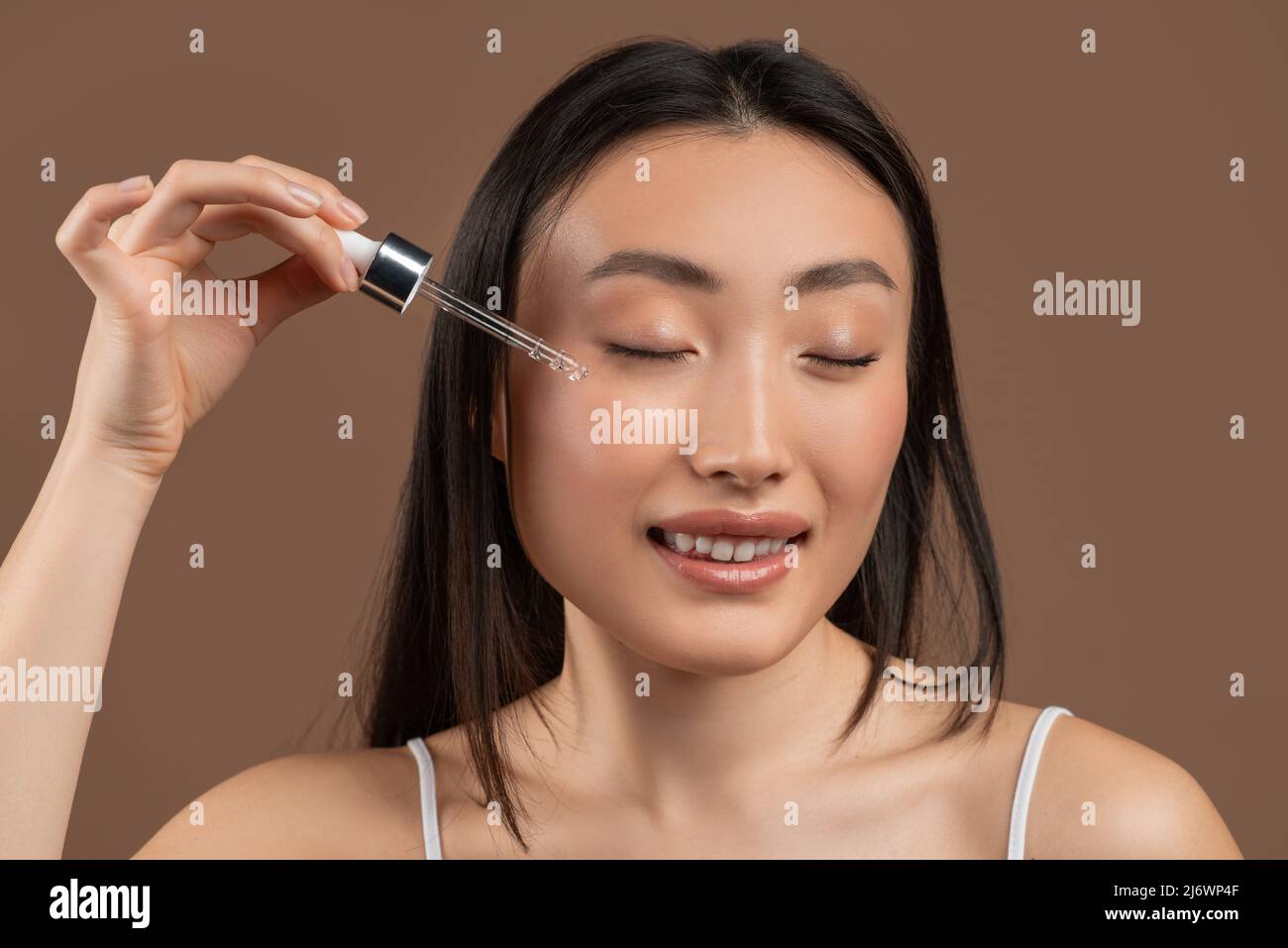 Happy korean lady holding pipette with hydrating facial serum, applying moisturizer or hyaluronic acid on face, closeup Stock Photo